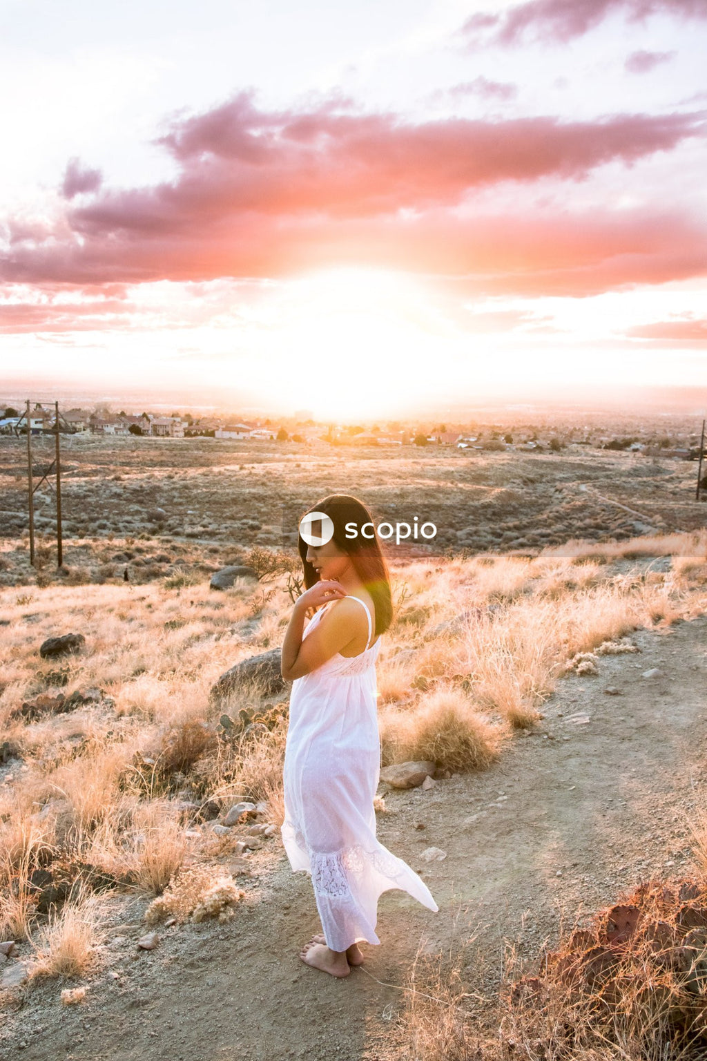 Woman in white tank top and white skirt standing on dirt road