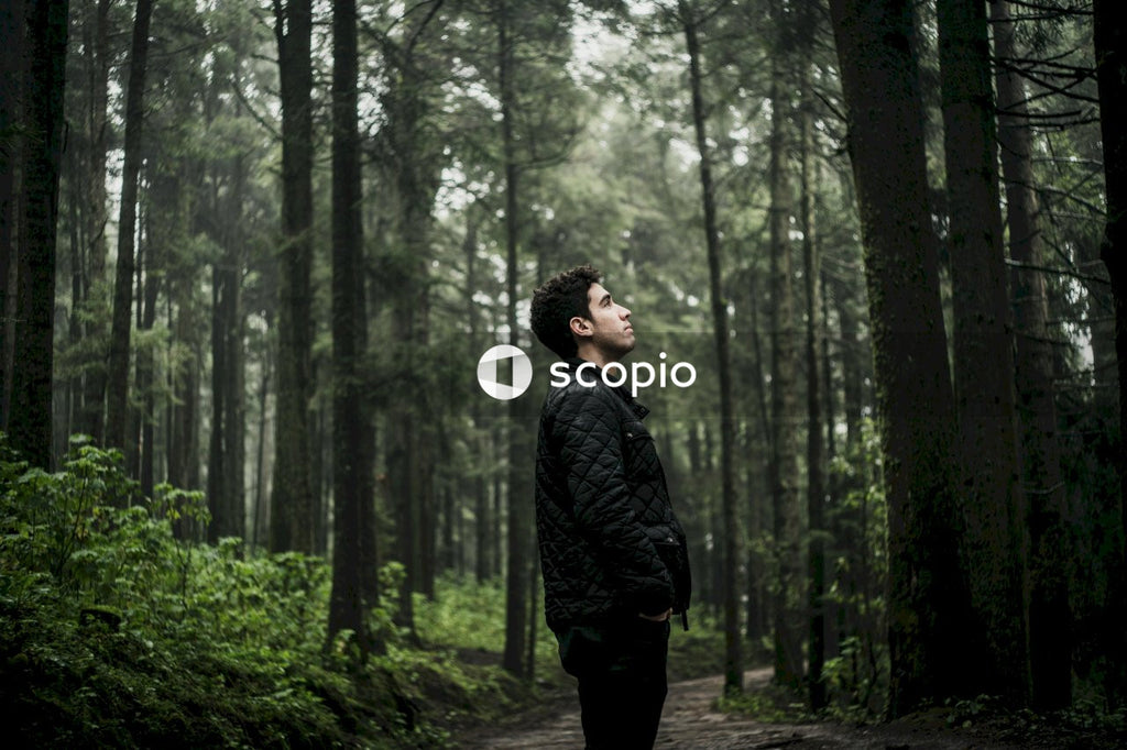 Side view of young man in leather jacket standing in the woods