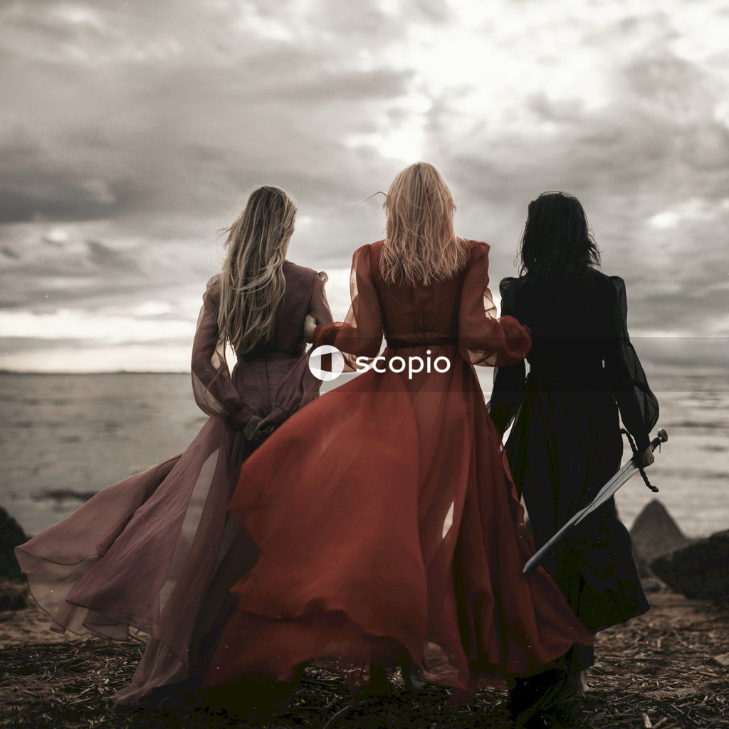 Three women in long dresses standing at the beach