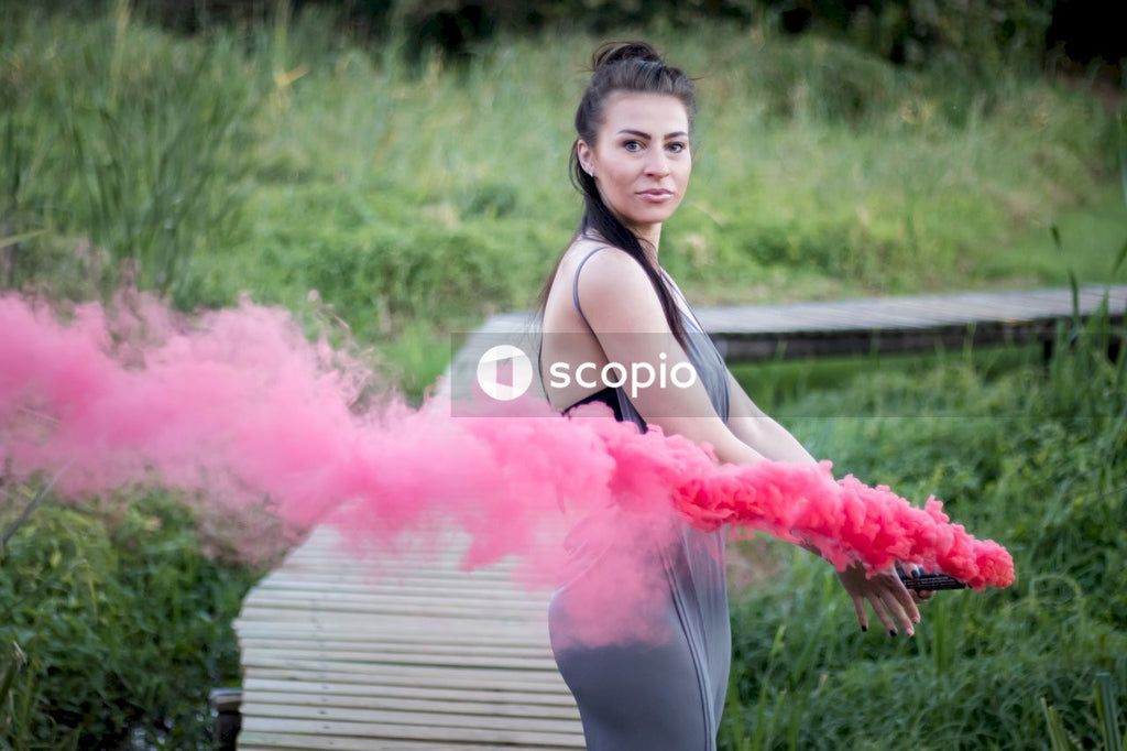 Woman in black tank top and white pants holding pink smoke