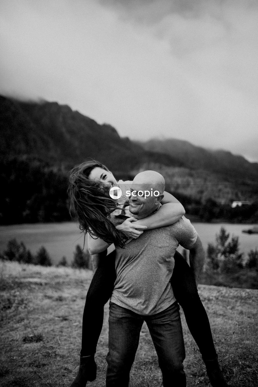 Grayscale photo of man holding woman on his back outdoor