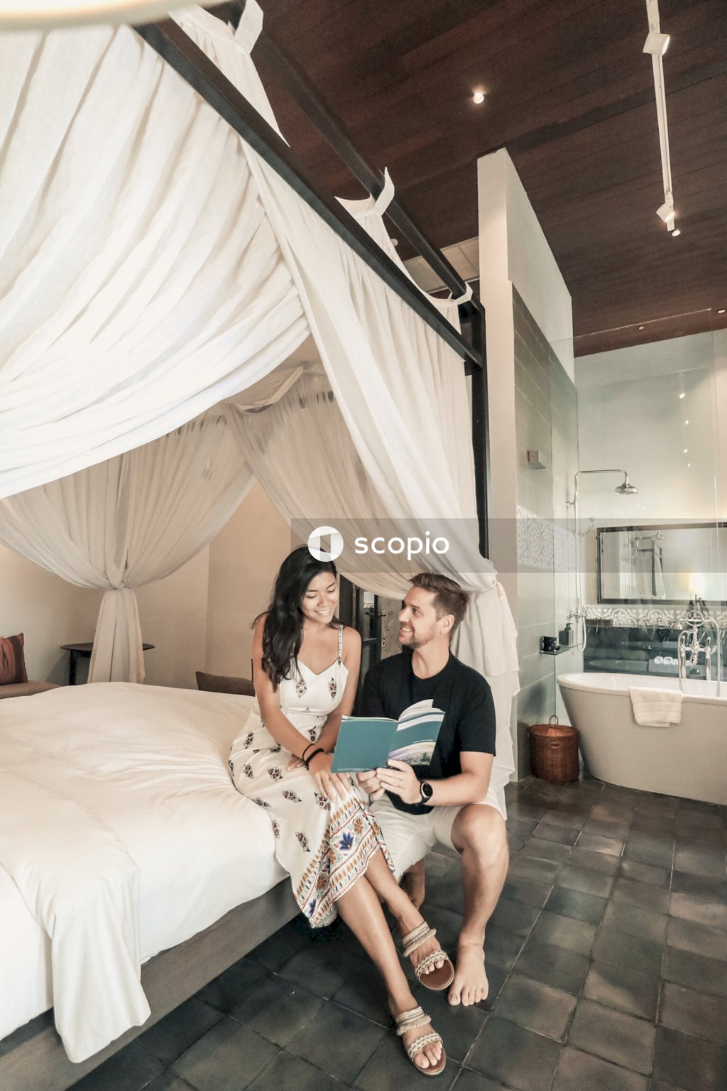 Young man and woman holding a book sitting on bed in a hotel room