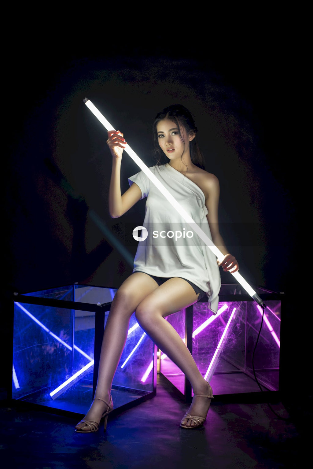 Woman holding neon light sitting on glass boxes