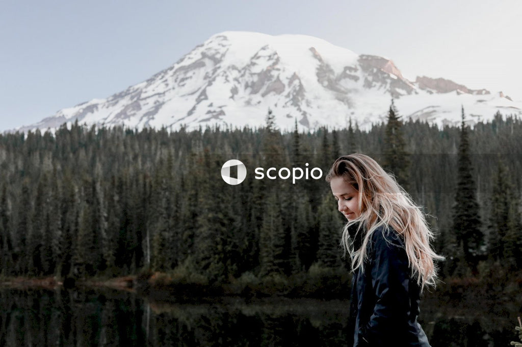 Woman in blue jacket standing near lake and snow covered mountain