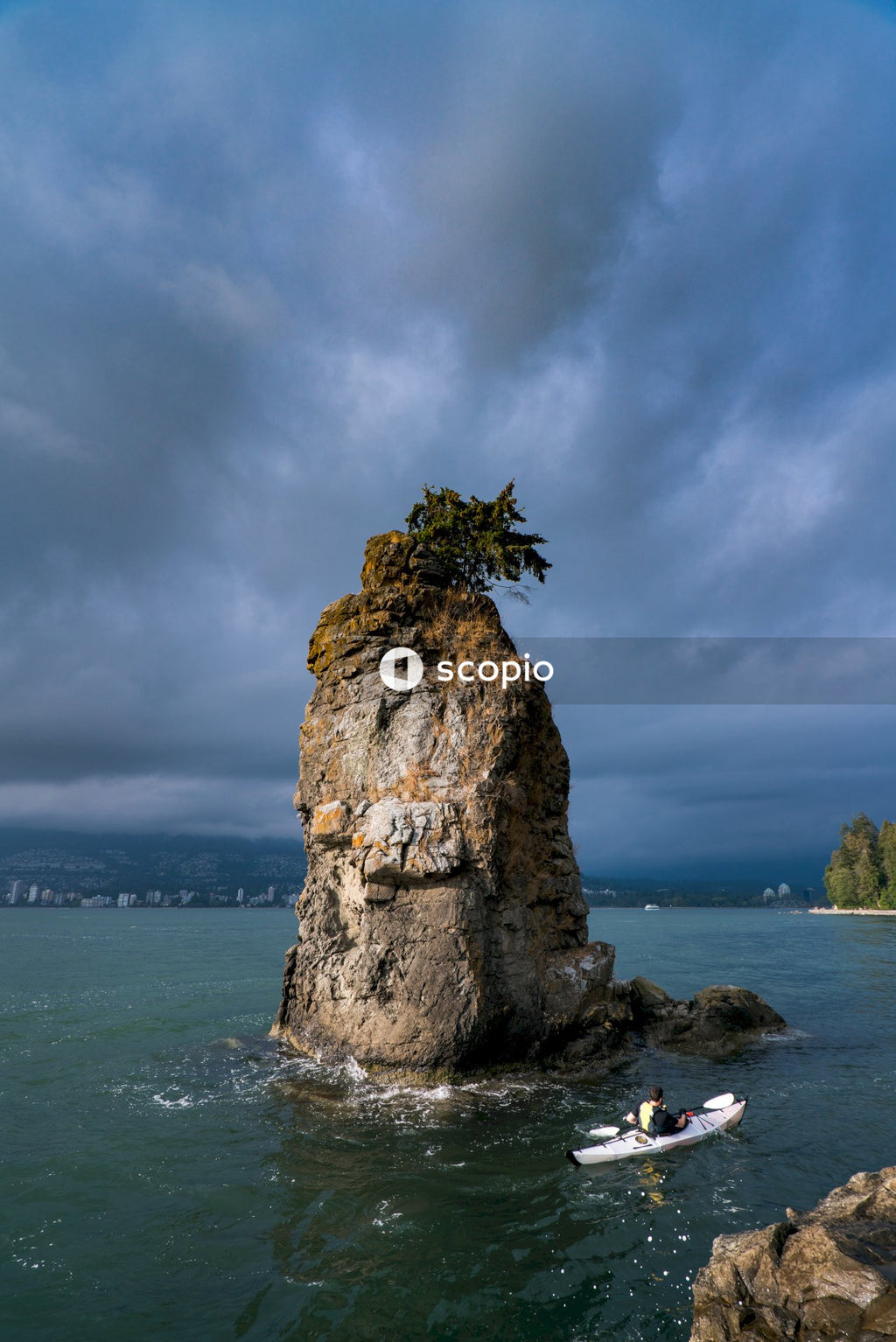 Person kayaking on boat near rock formation in the sea