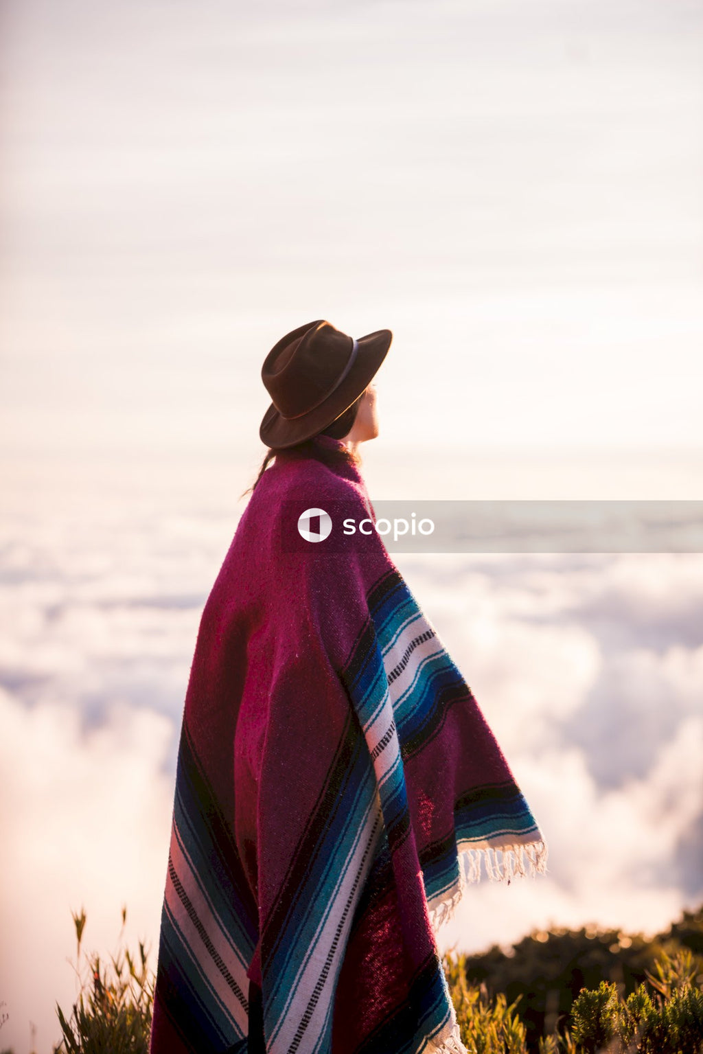 Woman in fedora hat and poncho standing above the cloud