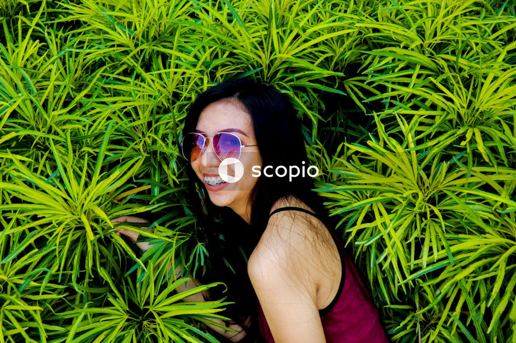 Portrait of woman with sunglasses and braces smiling beside green plants