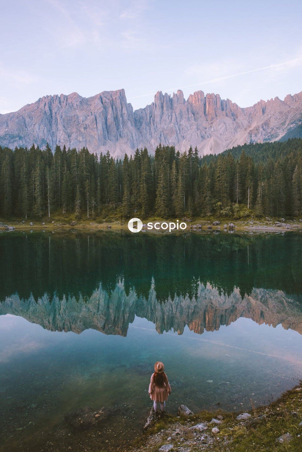 Back view of woman standing by waterside of lake Carezza in Dolomites in South Tyrol, Italy