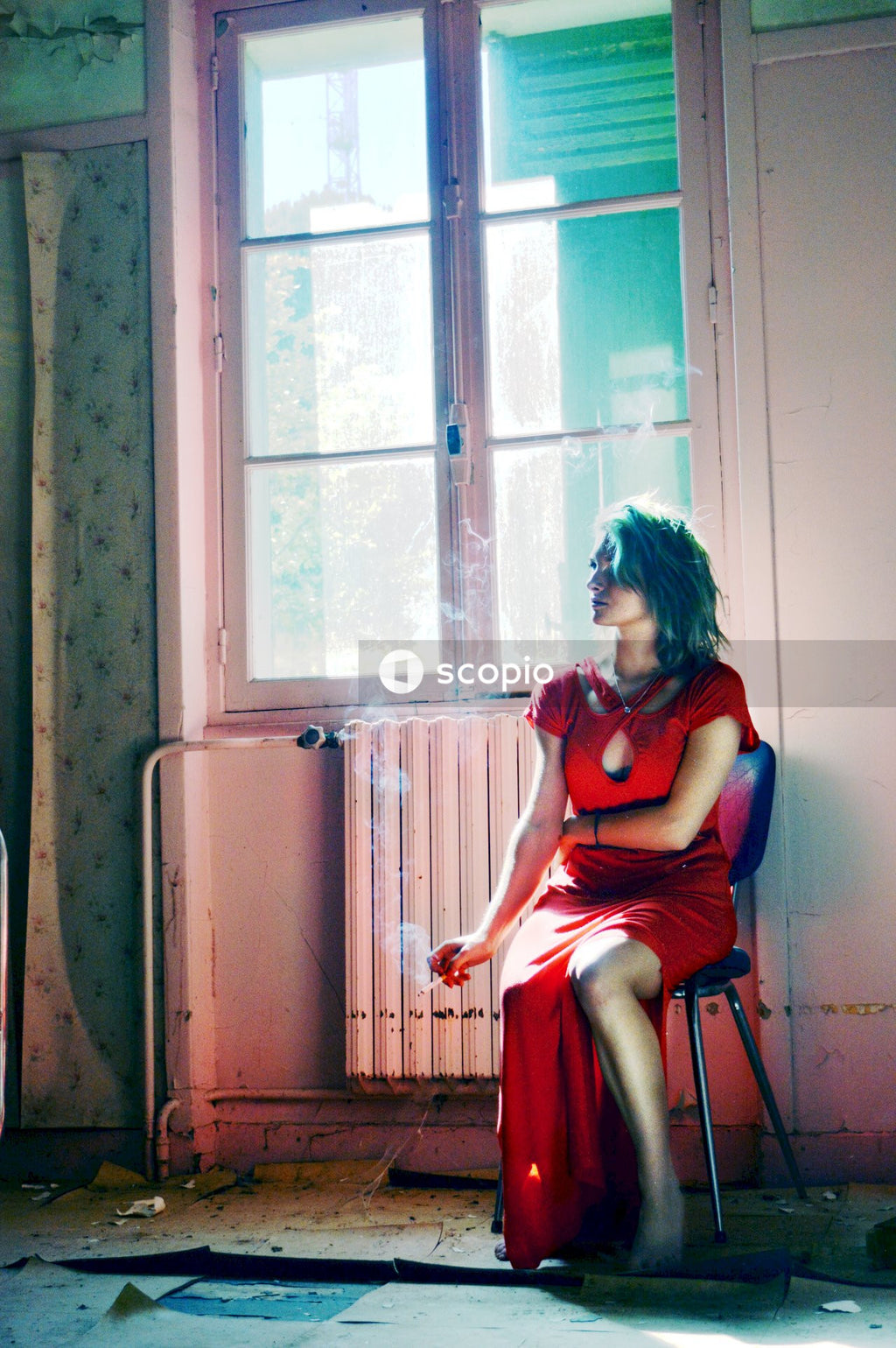 Woman in red dress sitting on chair next to window smoking