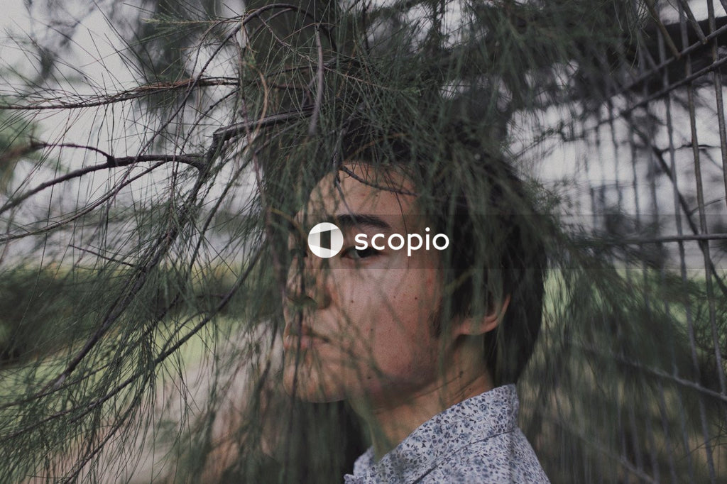 Man in grey and white shirt looking through tree twigs