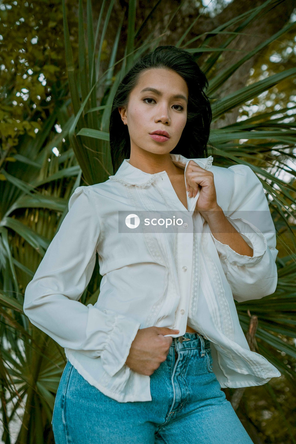 Woman in long sleeve shirt and blue denim jeans standing near green leaf plant
