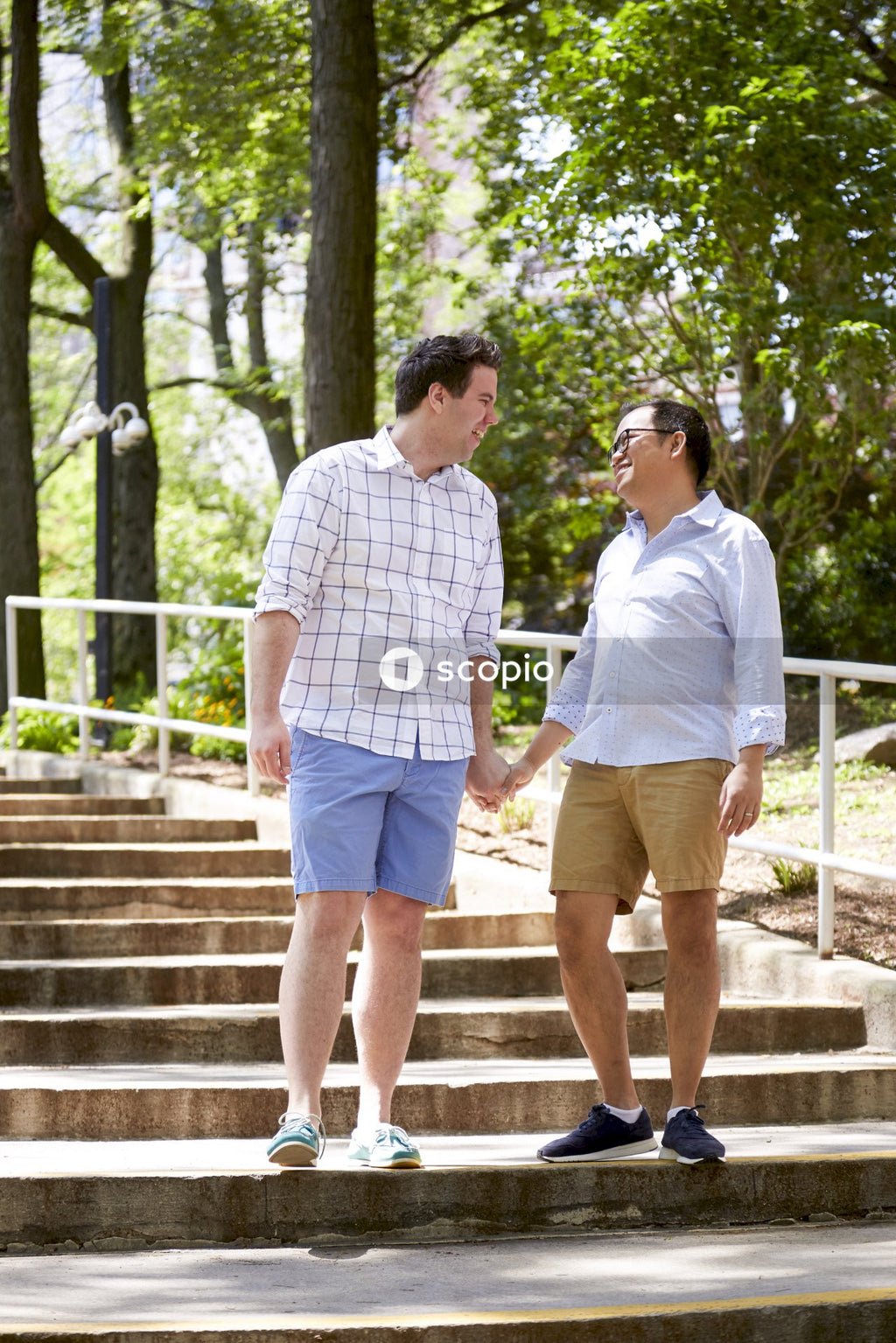Two smiling men holding hands and looking at each other standing on staircase
