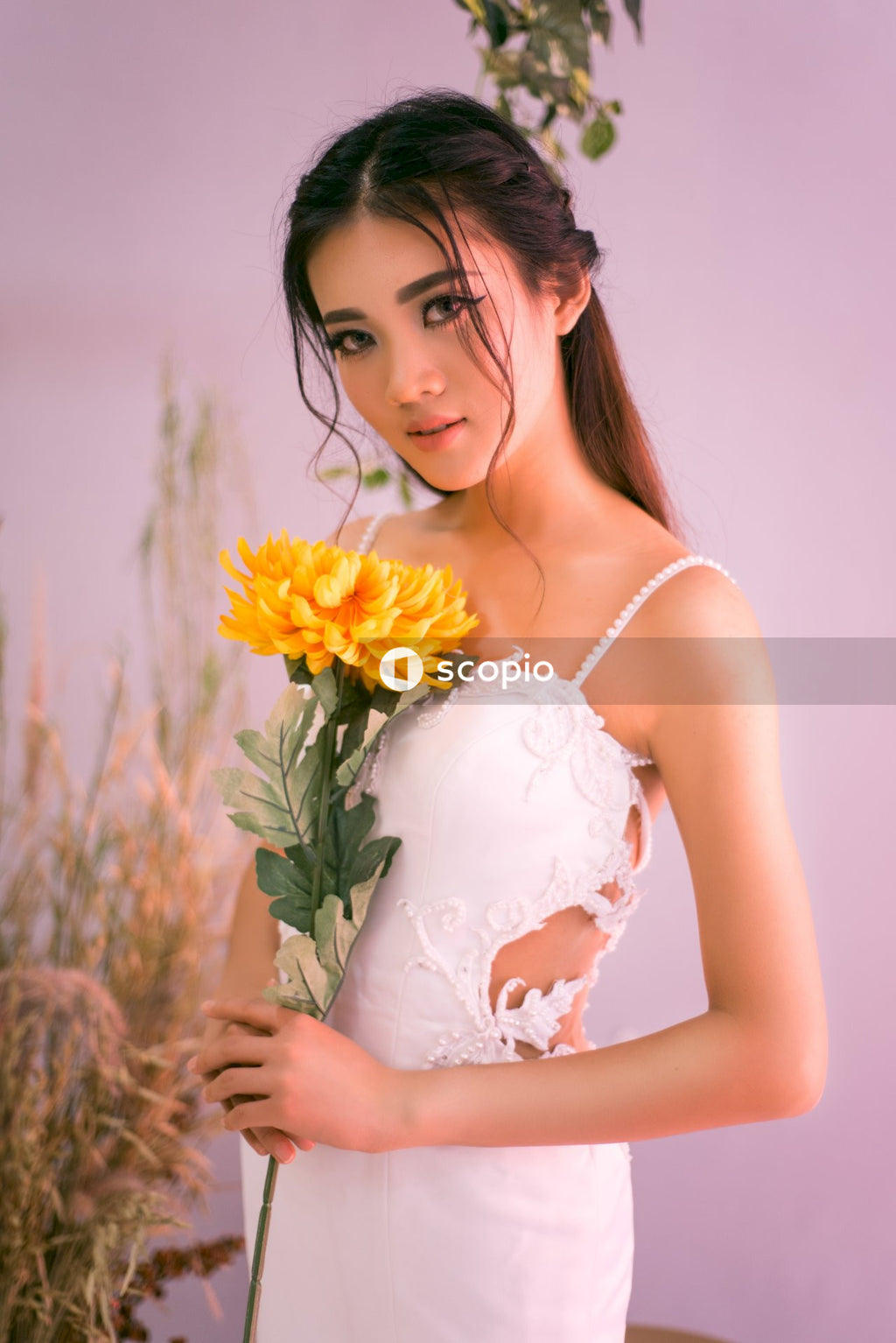 Young woman in long dress holding yellow flower bouquet indoor