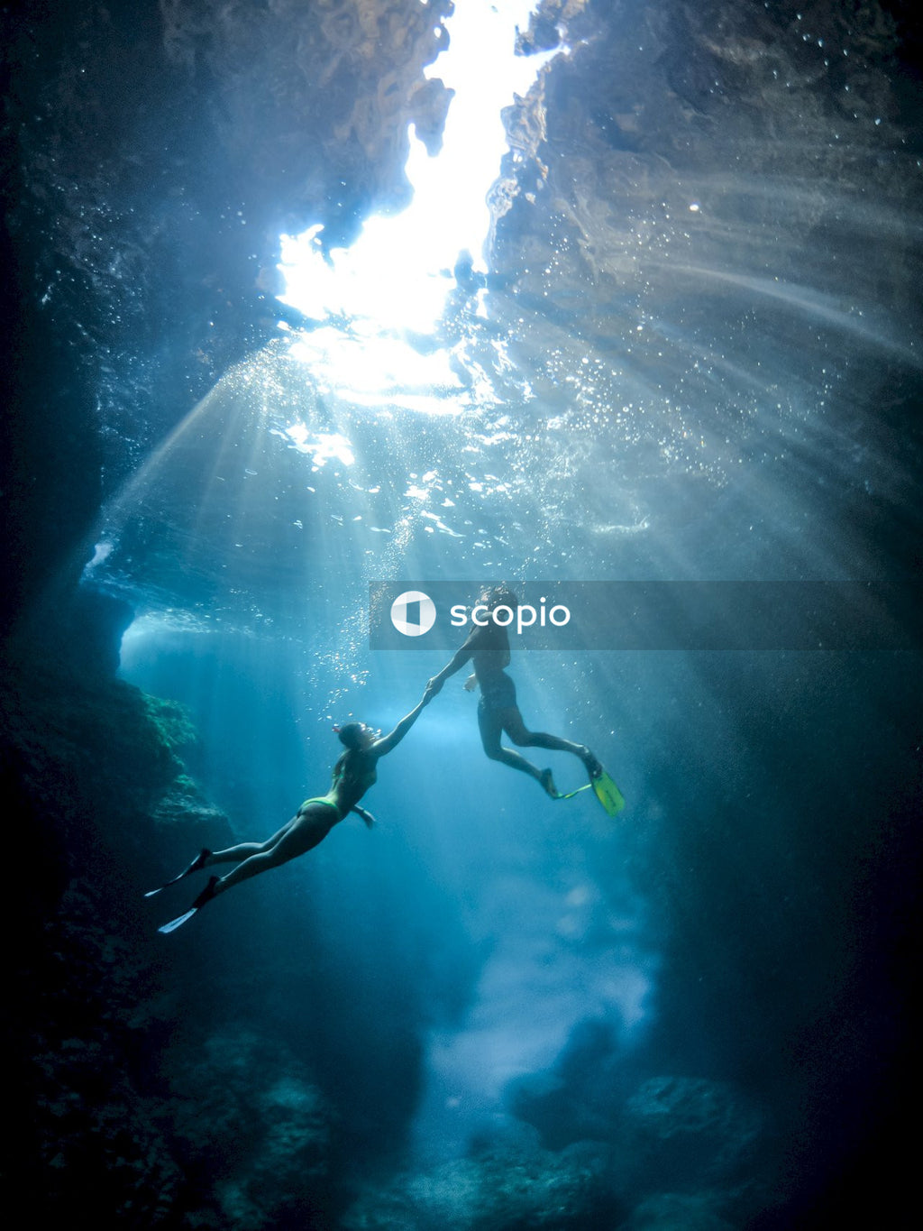 Underwater shot of man and woman diving in water and holding hands