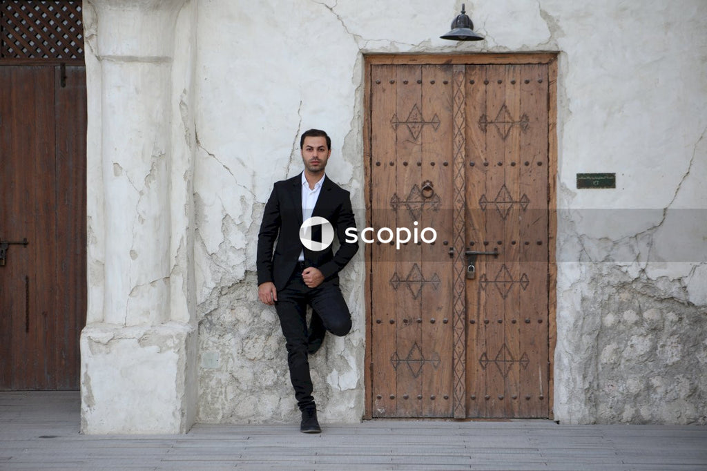 Man in black suit standing beside brown wooden door