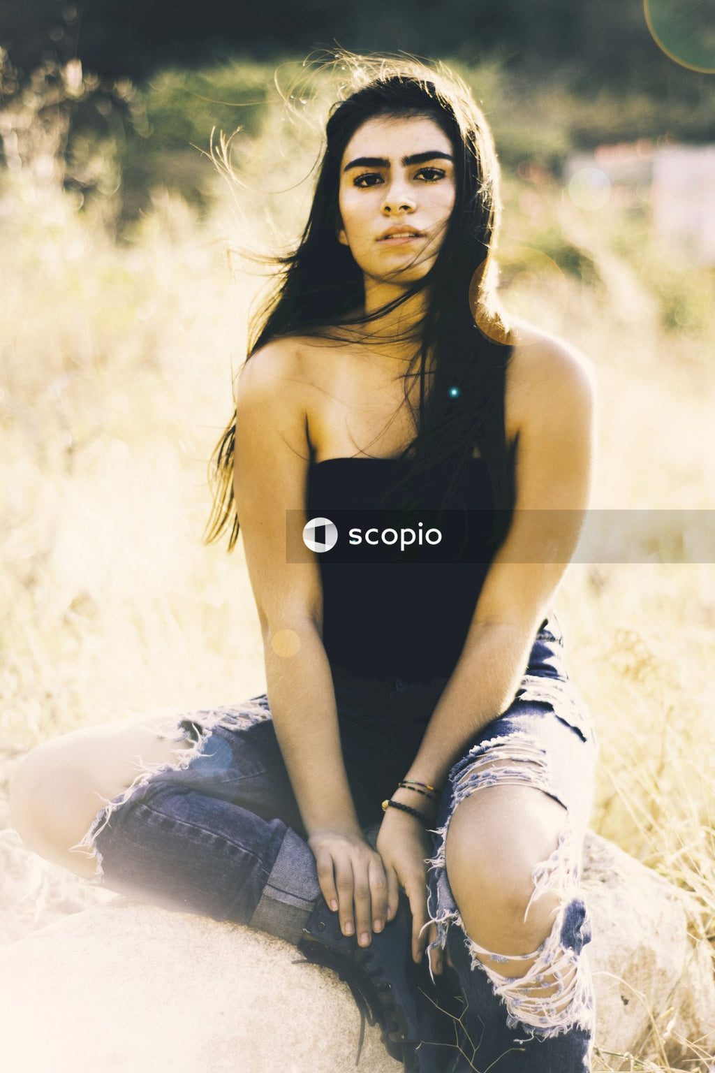 Portrait of woman in tank top and blue denim jeans sitting on ground outdoor