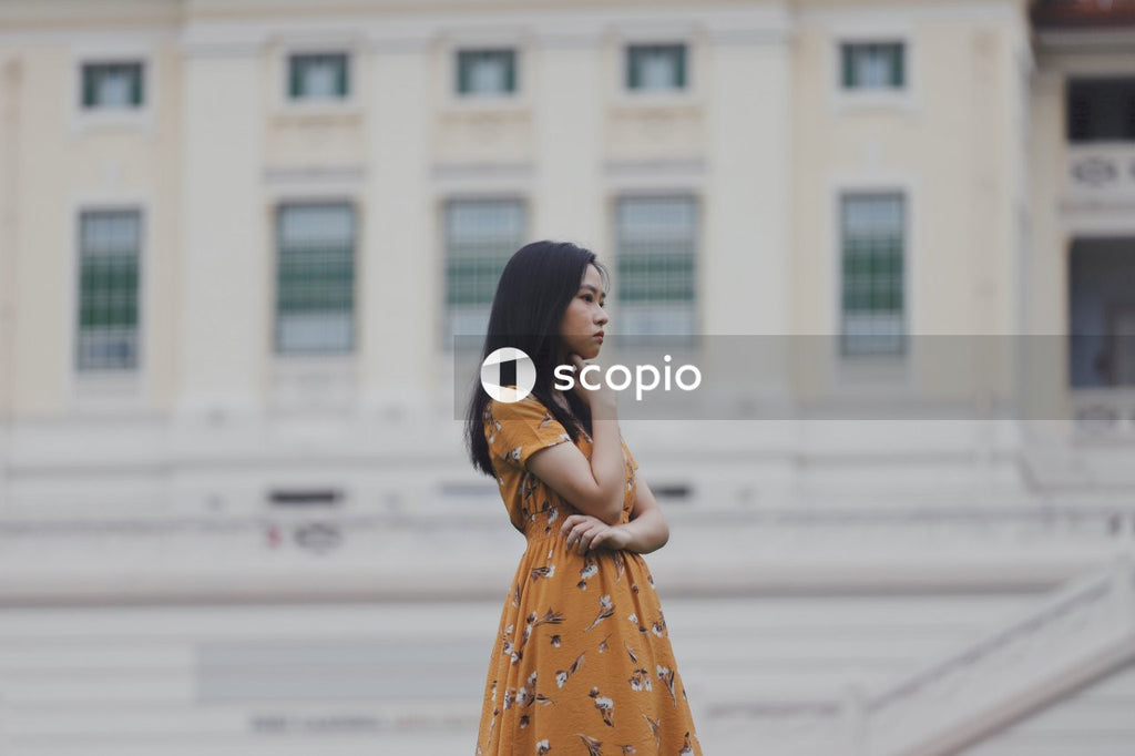 Woman in orange and white floral dress standing in front of light building