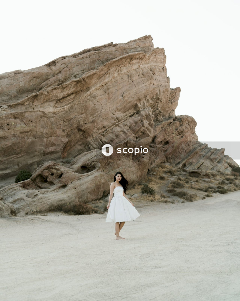 Woman in white dress standing on white sand near brown rock formation