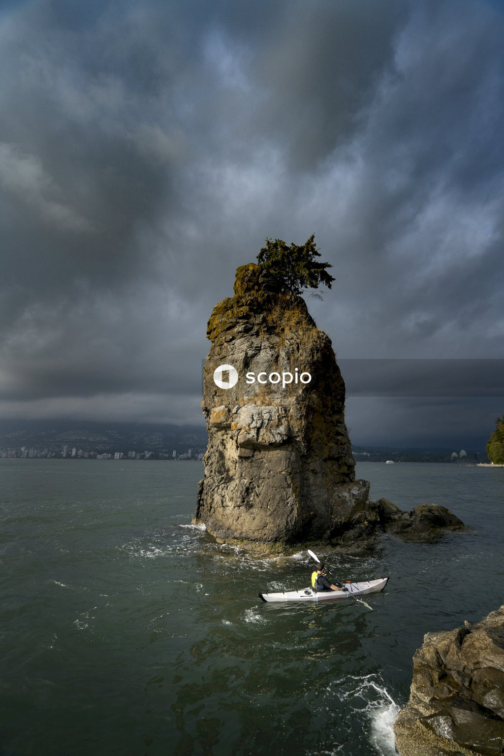 Person kayaking on boat near rock formation in the sea