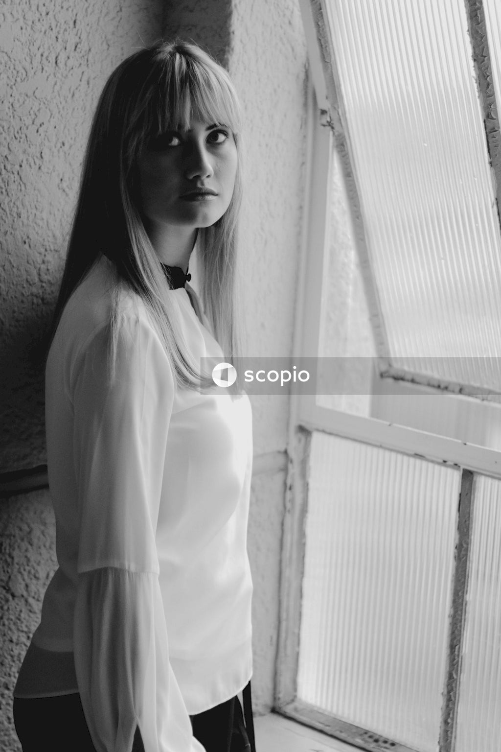 Woman in white long sleeve shirt standing beside window