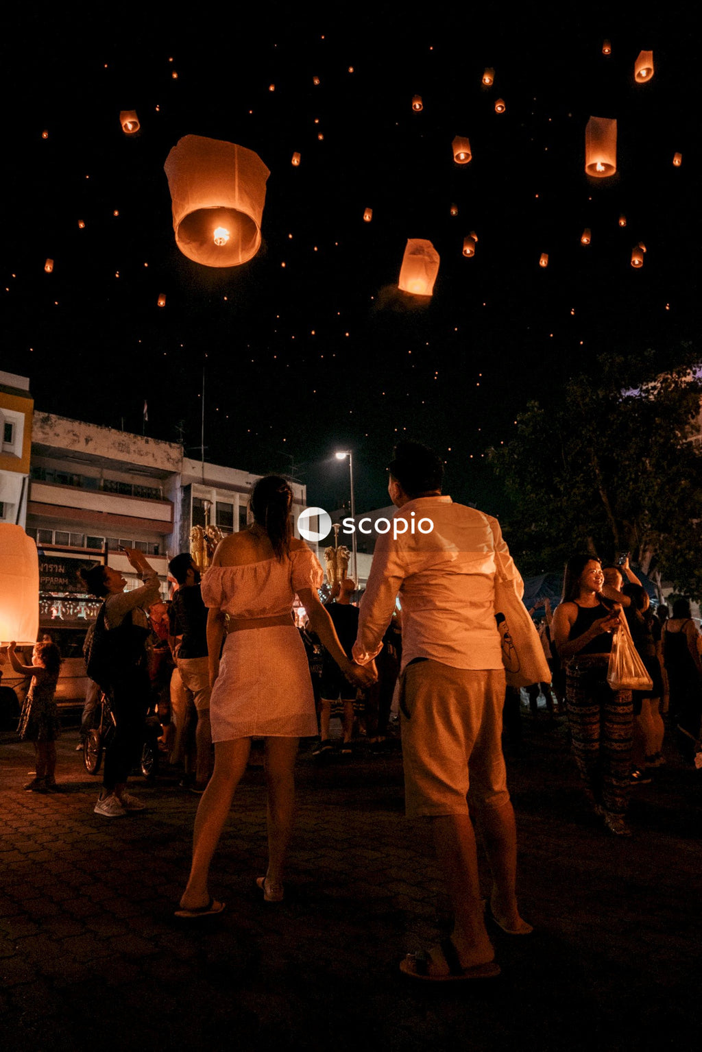 A couple holds hands as they watch lanterns float into the sky