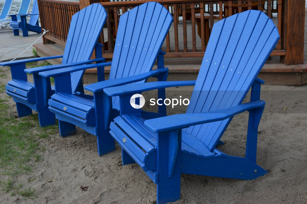 Blue wooden adirondack chairs on brown sand