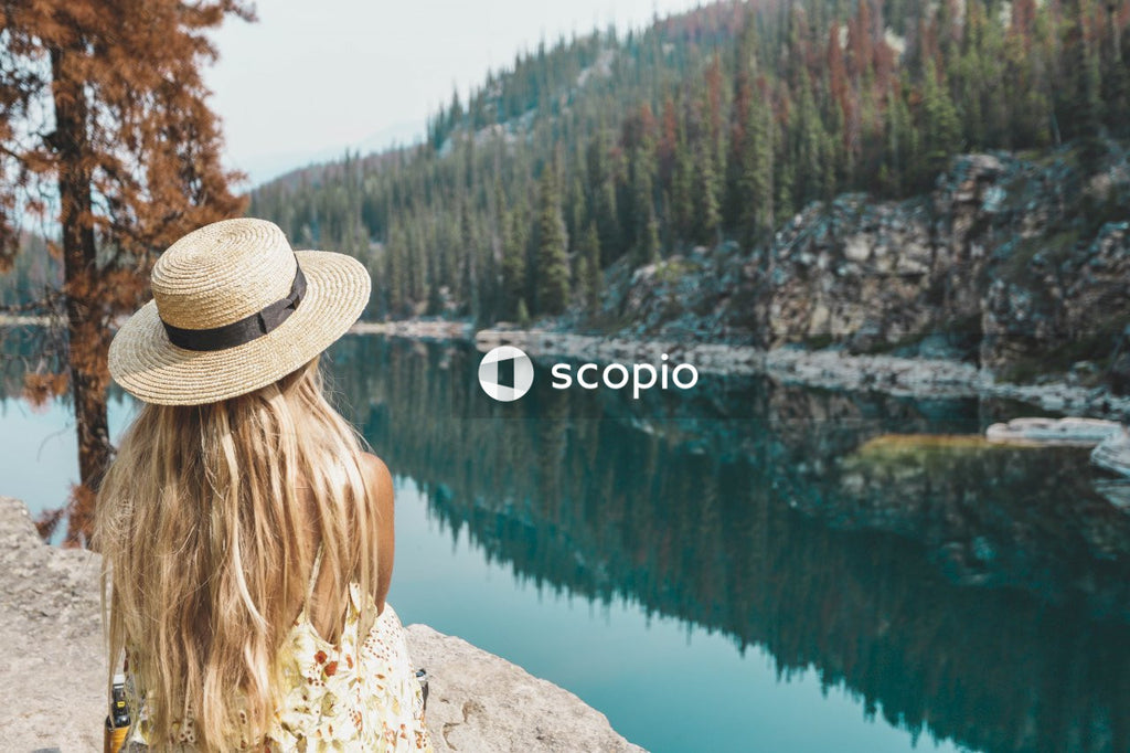 Woman in brown hat sitting on rock near lake