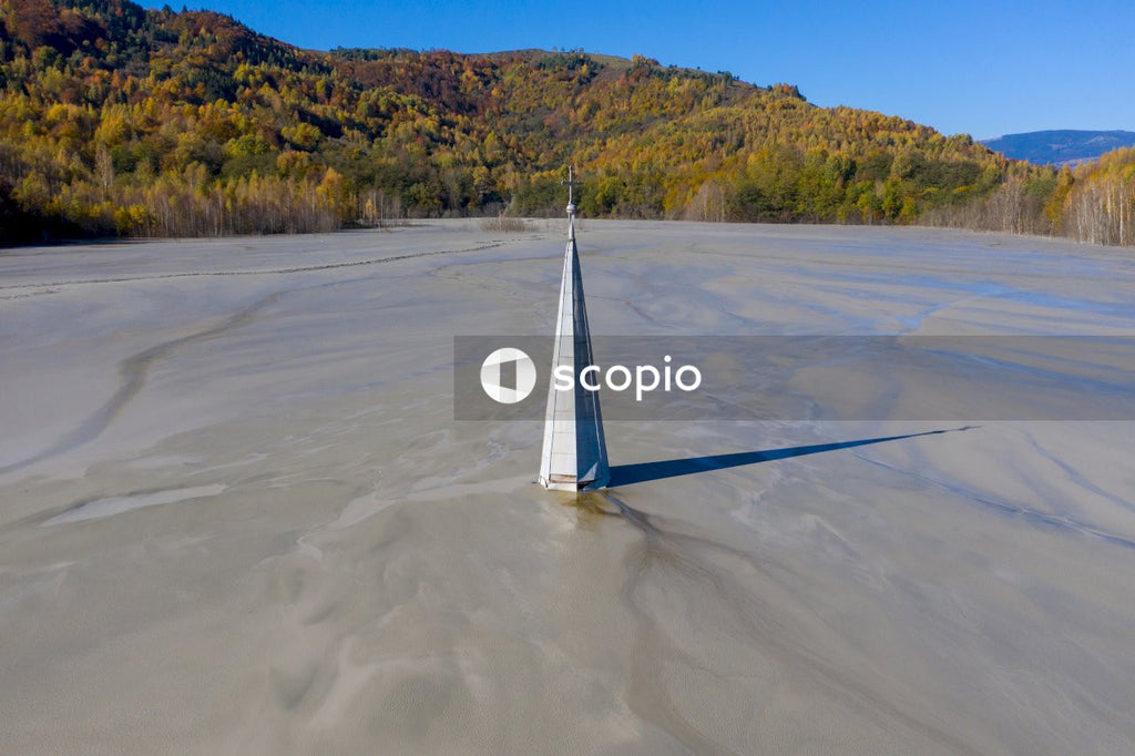 Aerial view of a church tower with cross, buried under mud and mining residuals. Apocalyptic scene in Transylvania, Romania