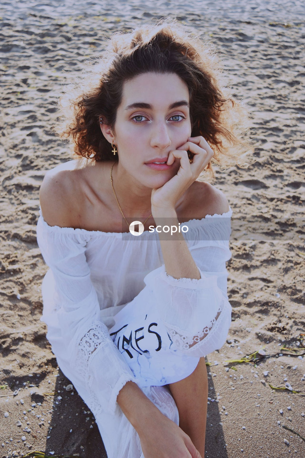 Young woman in light dress holding a handwritten paper with "Time's Up" at the beach