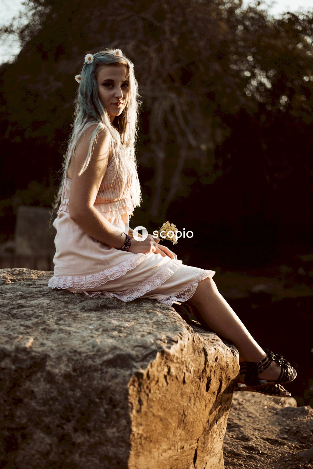 Woman in white sleeveless dress sitting on brown rock