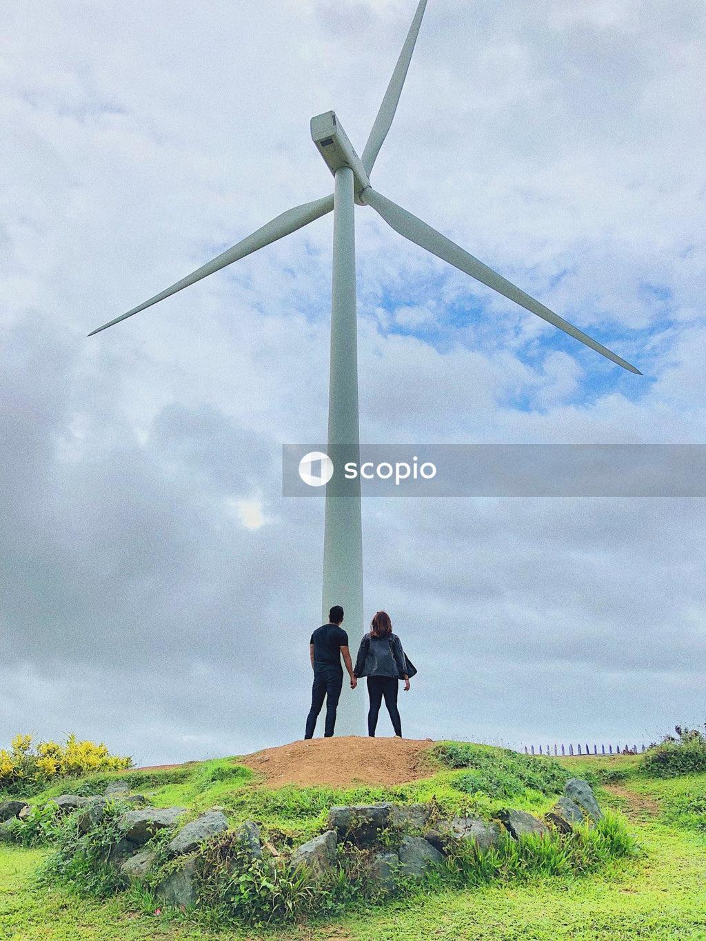 Man and woman holding hands and standing beside wind turbine