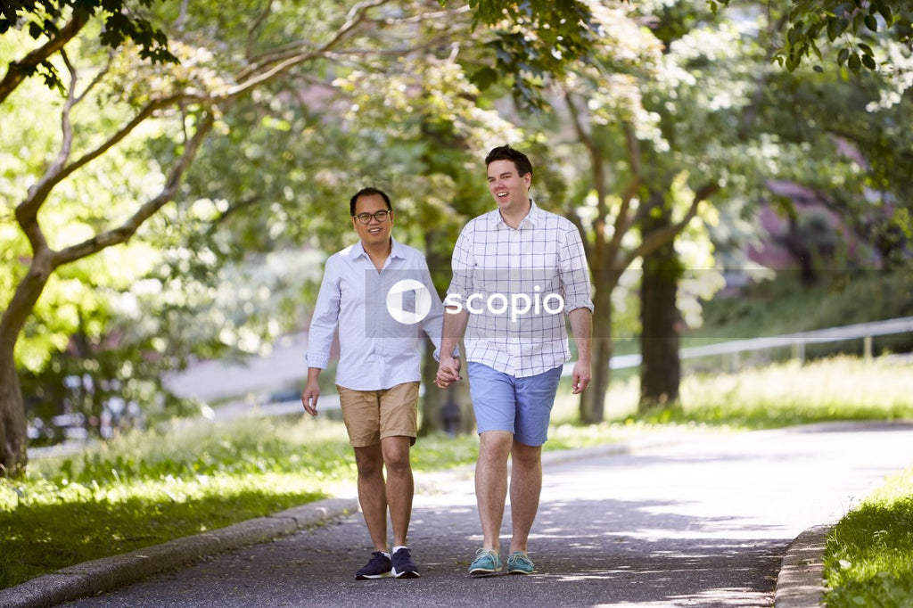Two men holding hands and walking between trees in the park