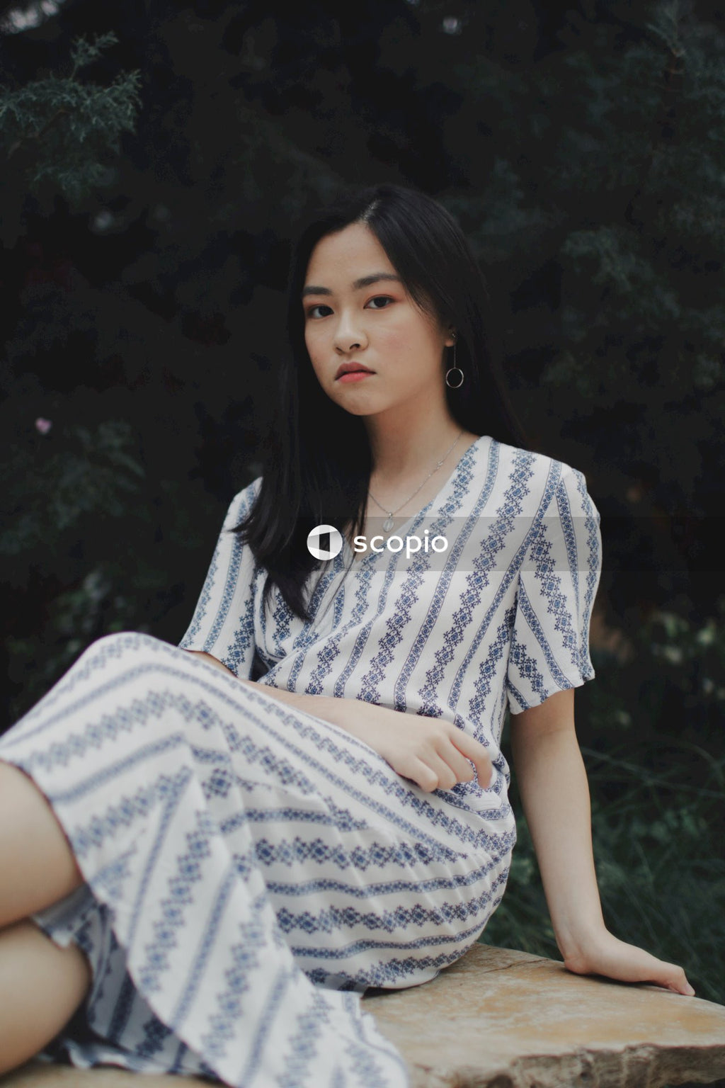 Woman in long light and blue stripped dress posing near bushes and flowers