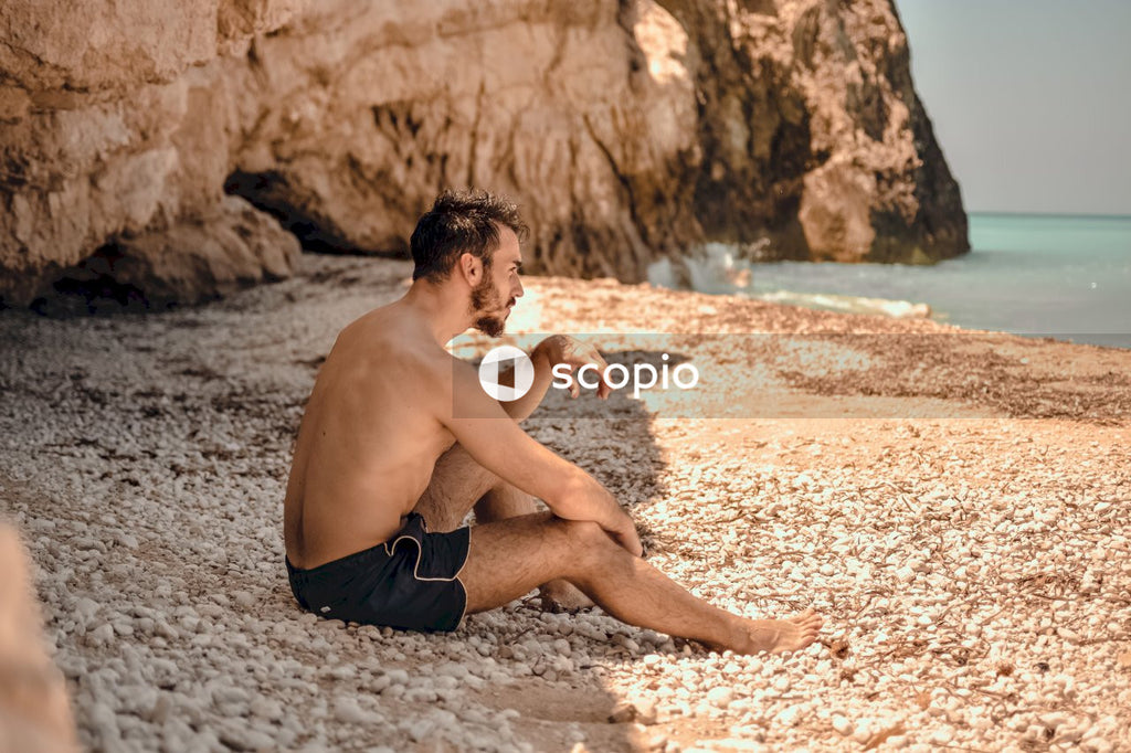 Man in shorts sitting on sand at the beach looking away