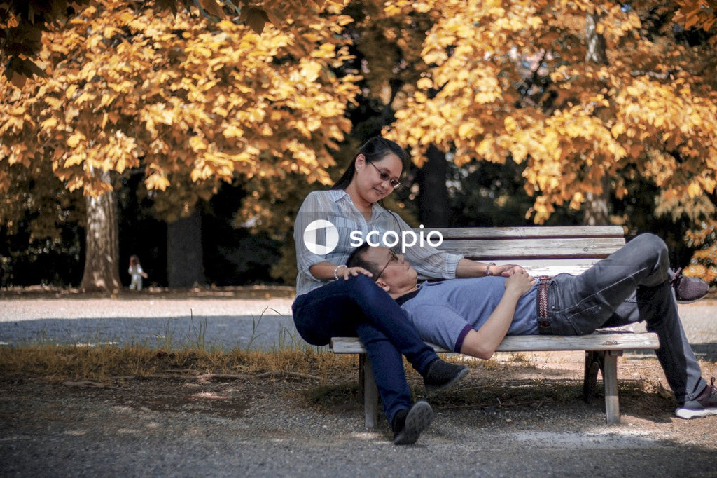 Man leaning his head on woman's lap sitting on brown wooden bench