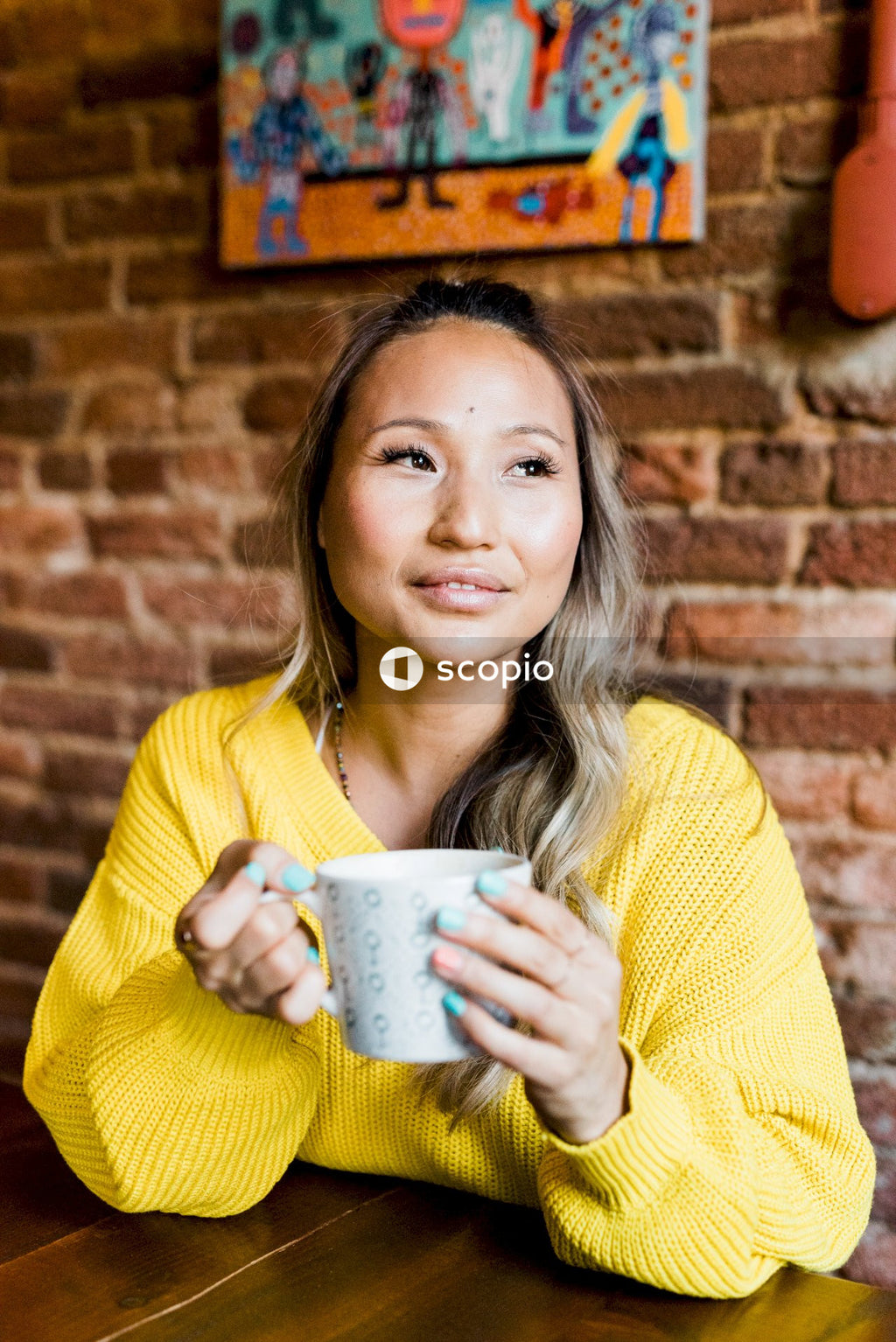 Woman in yellow sweater holding ceramic mug sitting at a table indoor
