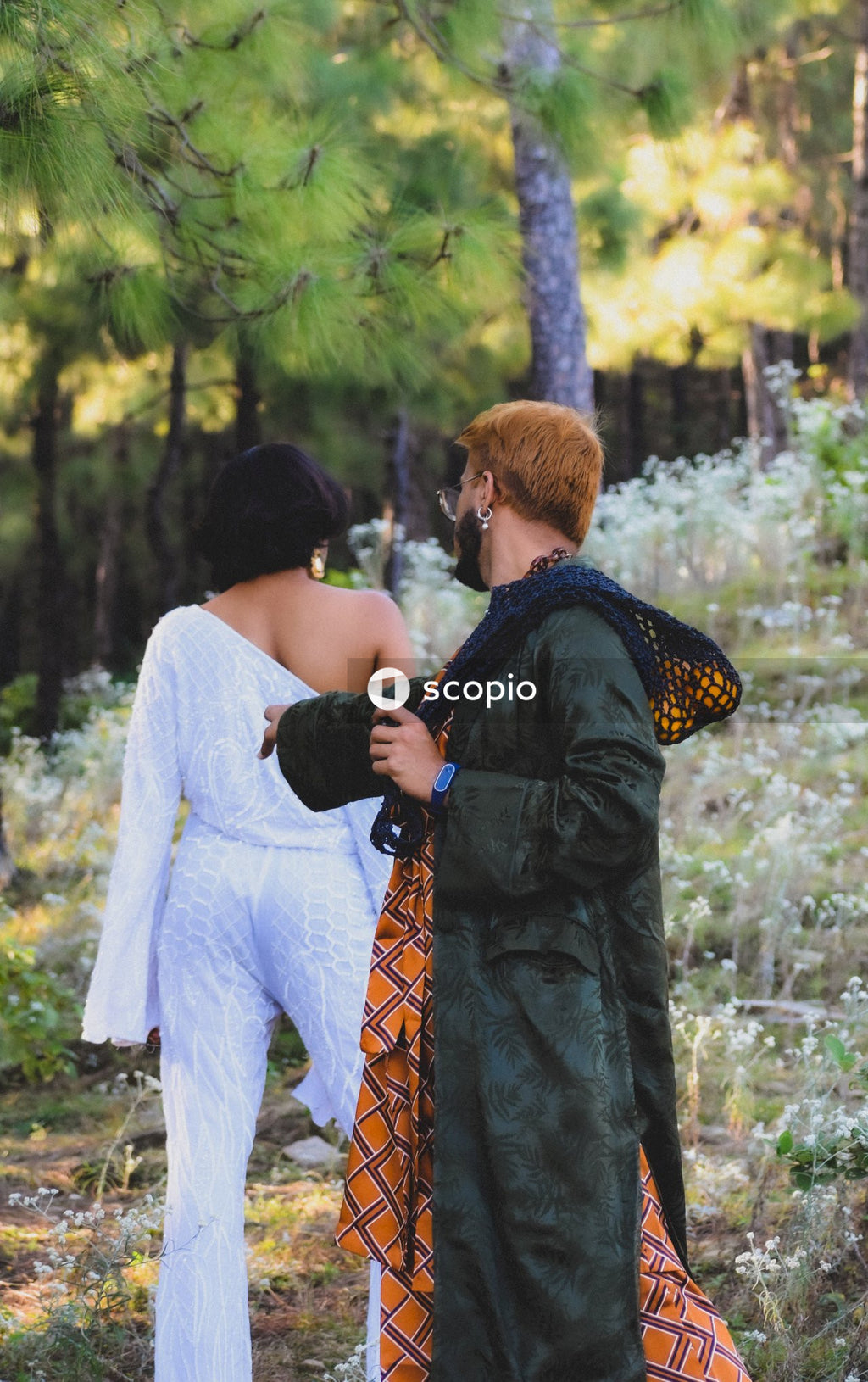 Back view of a man with camera reaching out his had to genderqueer model posing in a light jumpsuit outfit