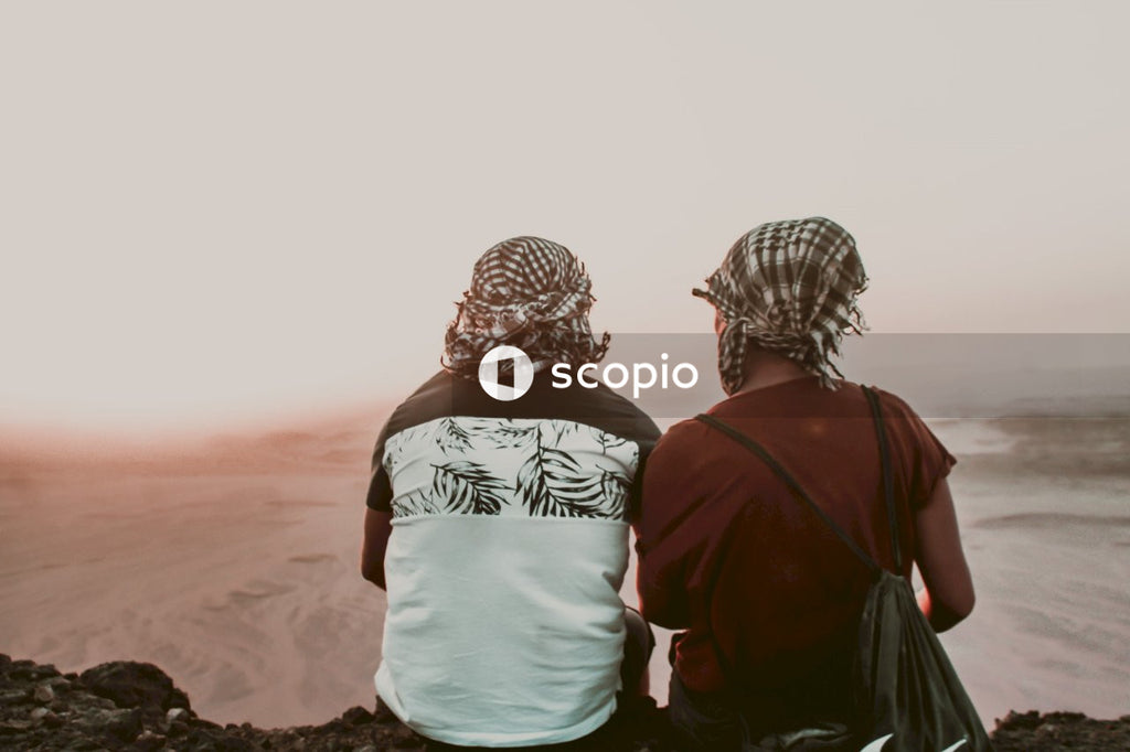 Back view of man and woman with Shemaghs sitting in desert