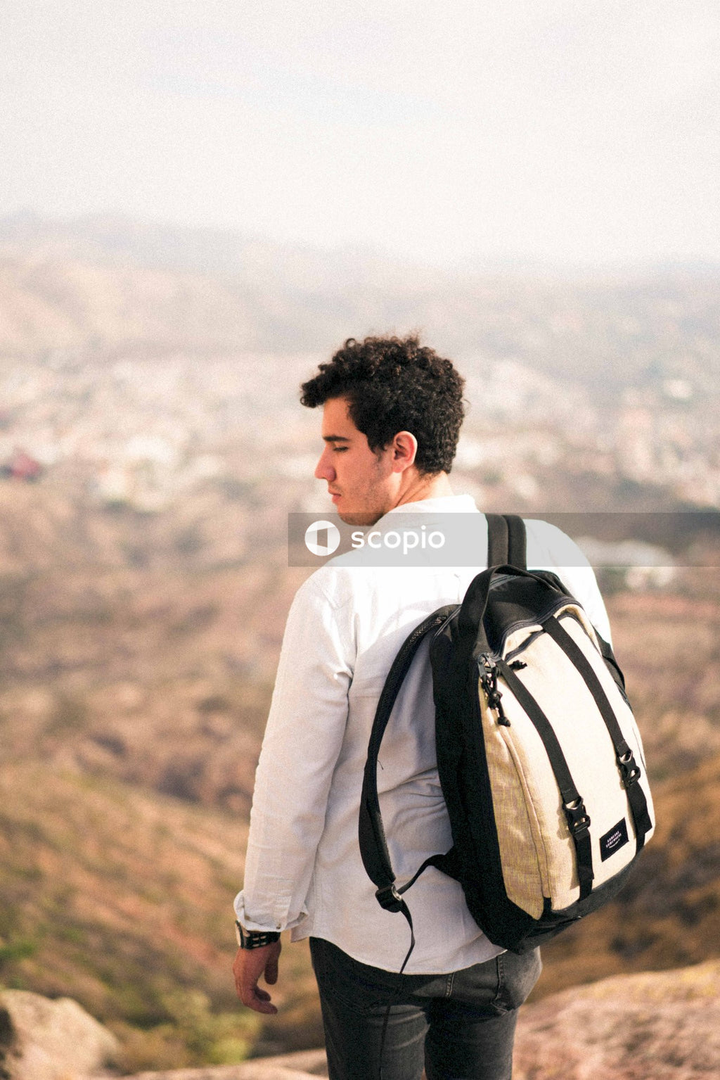Back view of man with backpack standing against natural landform
