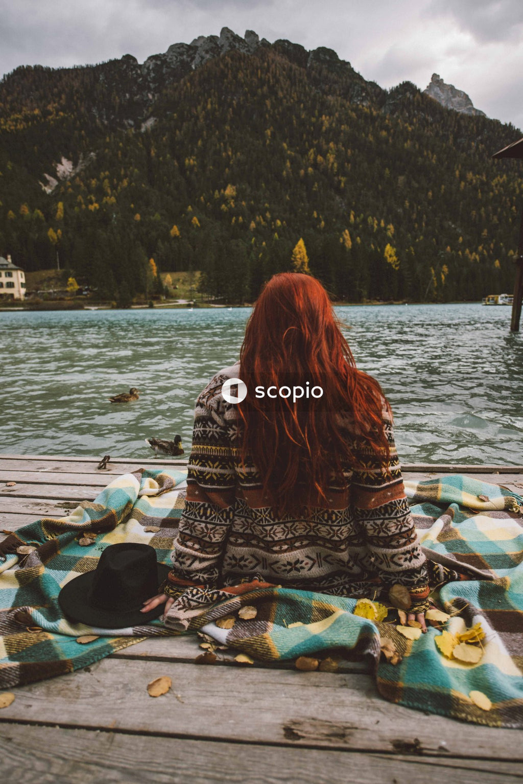 Back view of woman sitting on textile on wooden dock by the lake