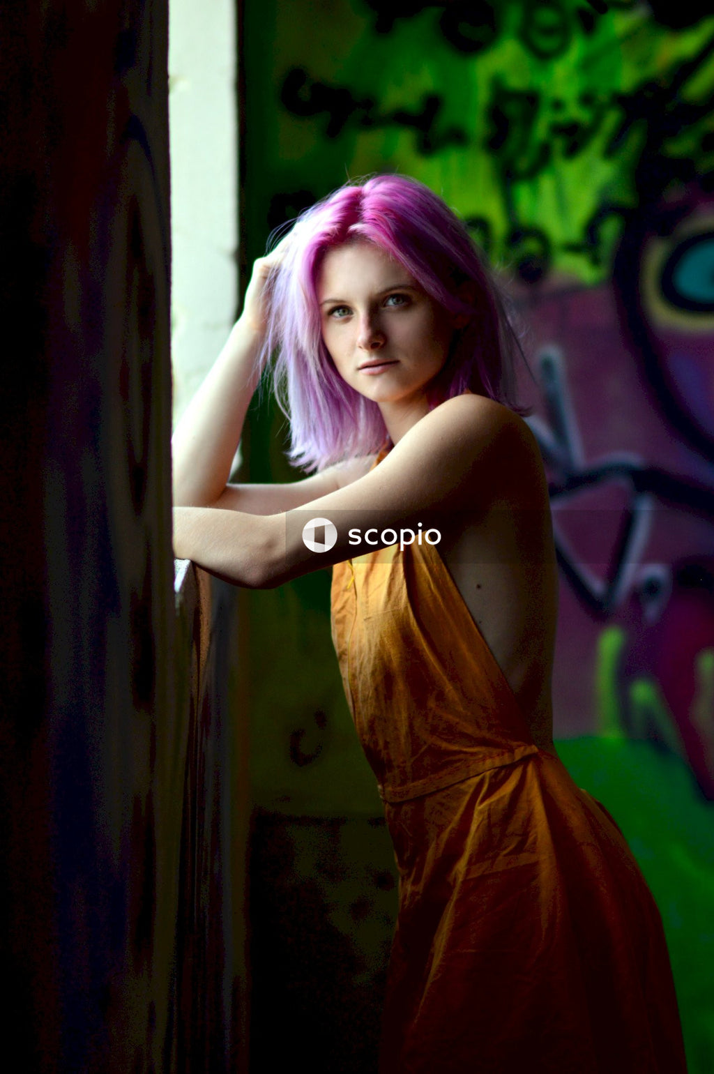 Woman with pink hair in yellow dress leaning on window
