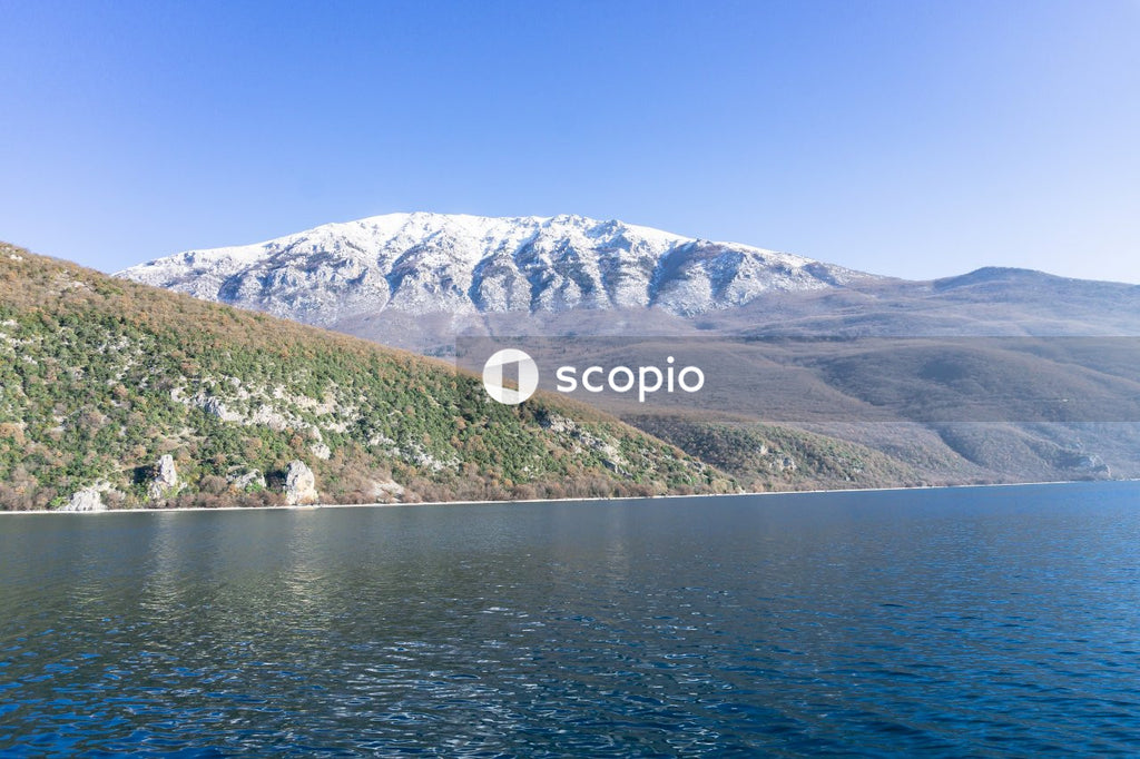 Green and white mountain beside body of water under blue sky