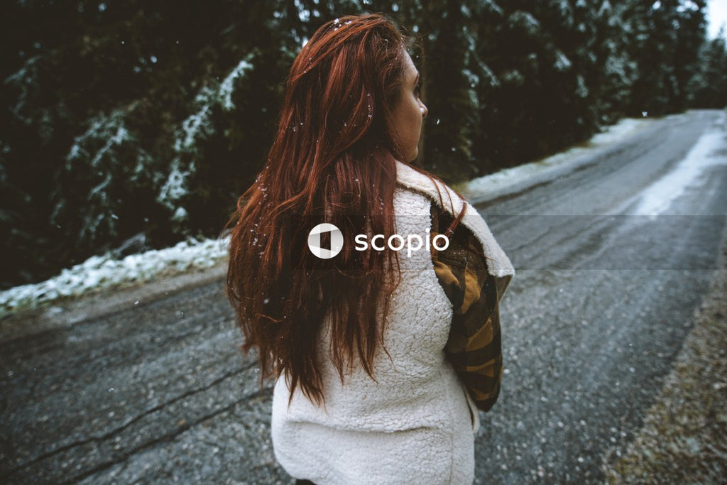 Back view of woman with red hair standing on snow covered road