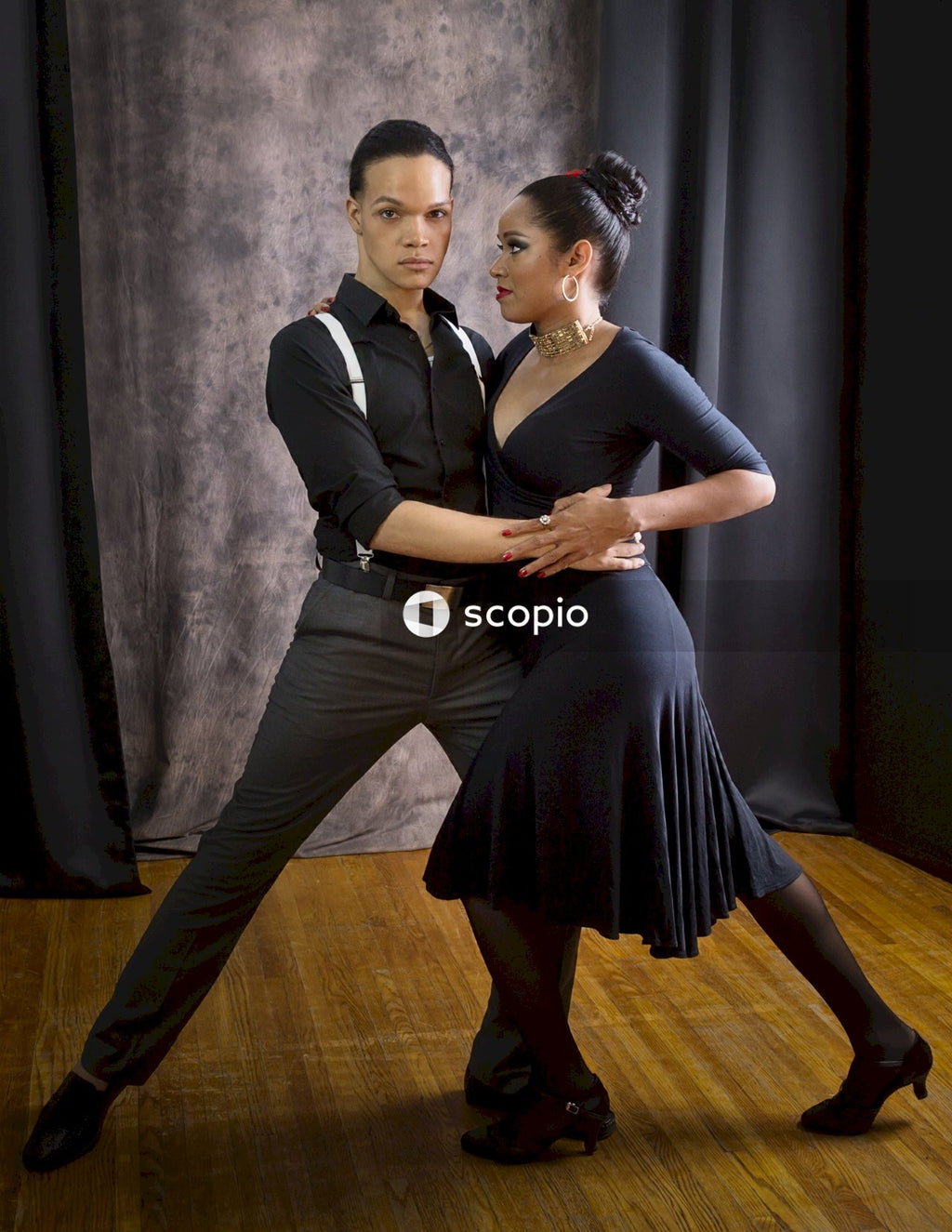 Man in black vest and black dress pants hugging woman in black dress