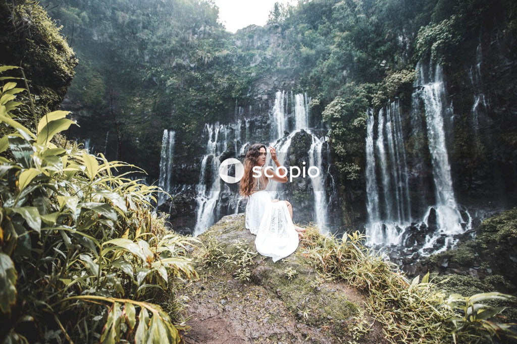 Woman in white dress standing on brown soil near waterfalls