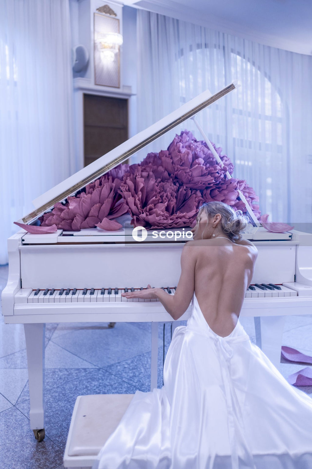 Beautiful woman with white piano and peonies flowers in white studio