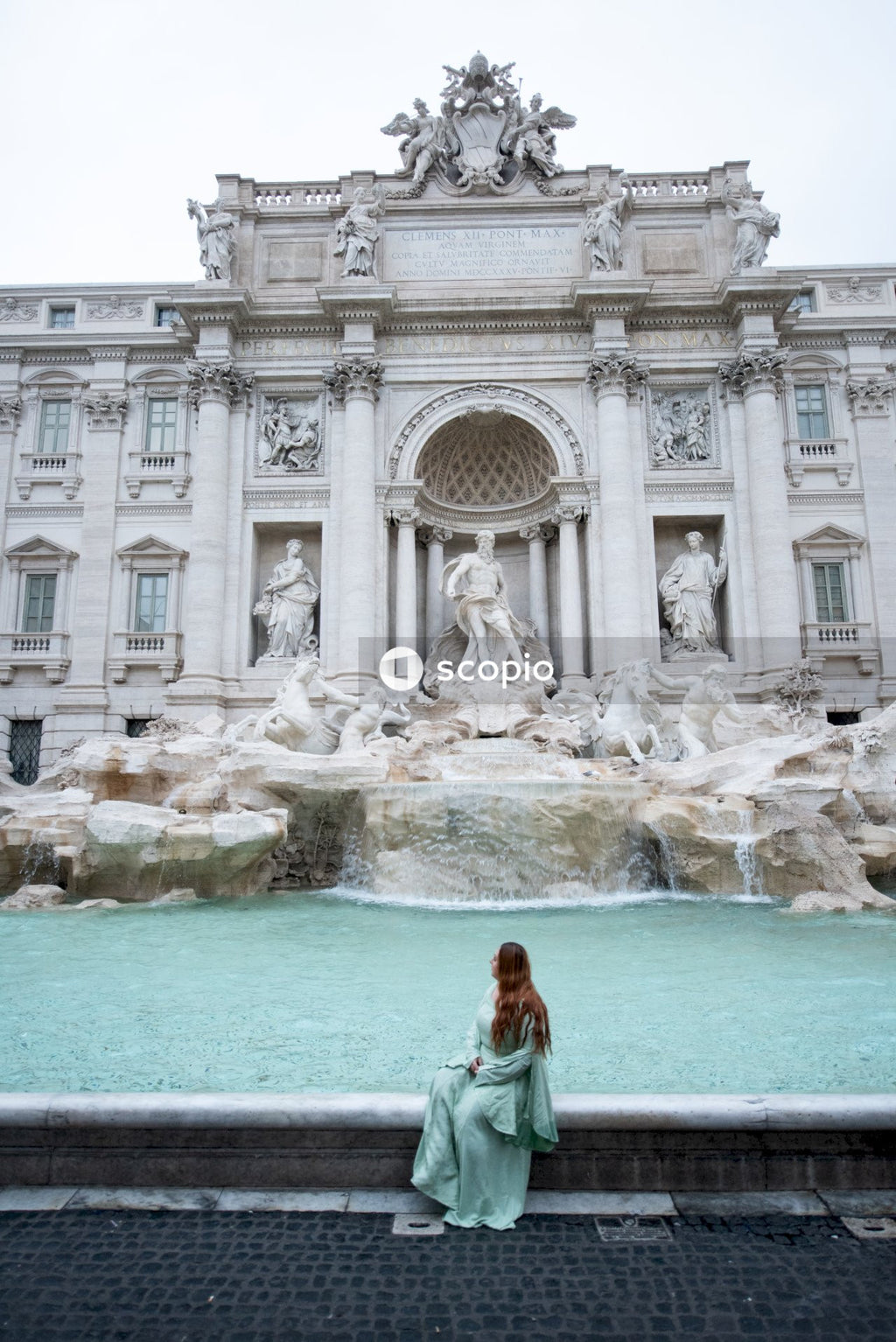 Woman in teal long sleeve shirt standing in front of fountain