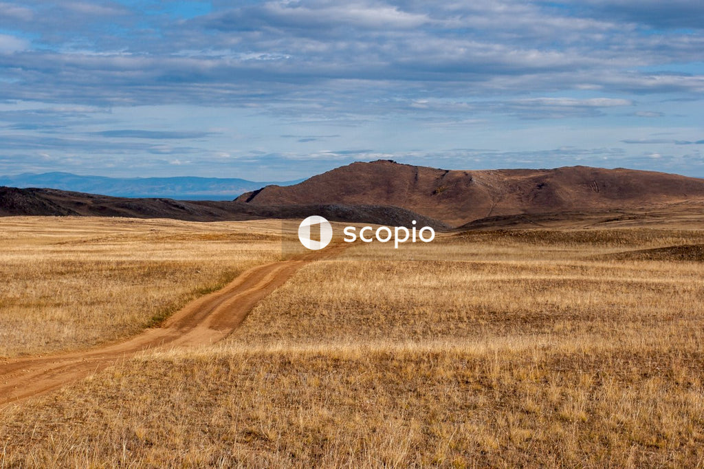 Brown grass field near brown mountain under blue sky