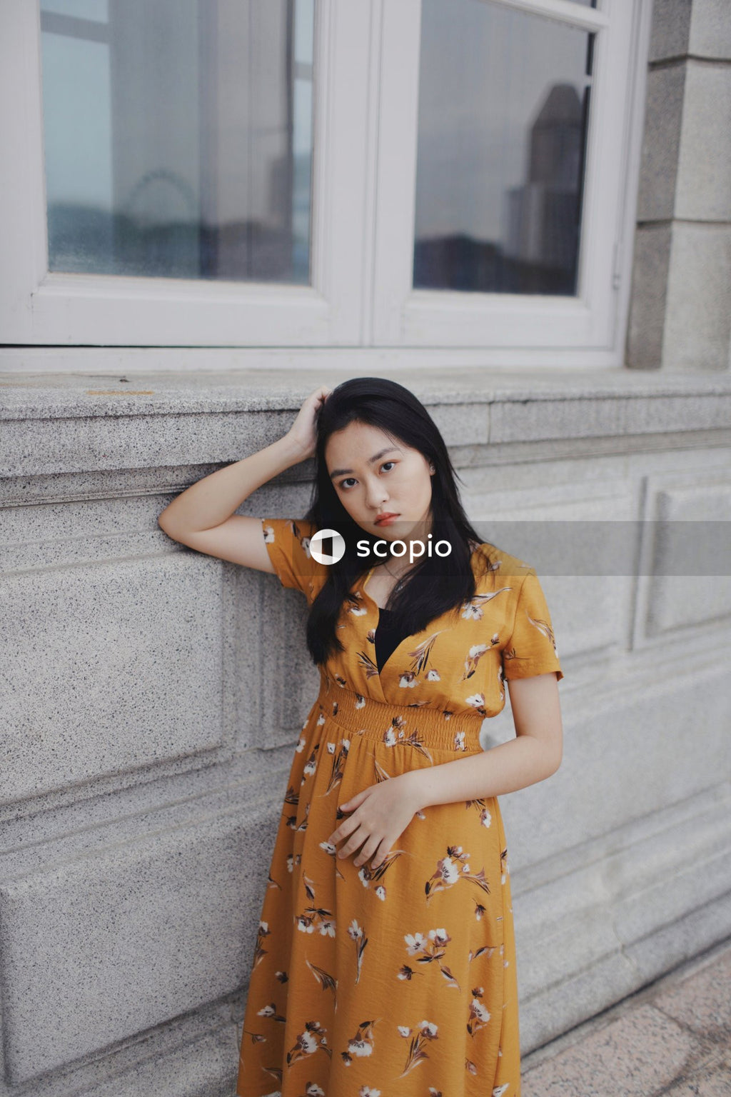 Woman in long orange dress leaning on light wall