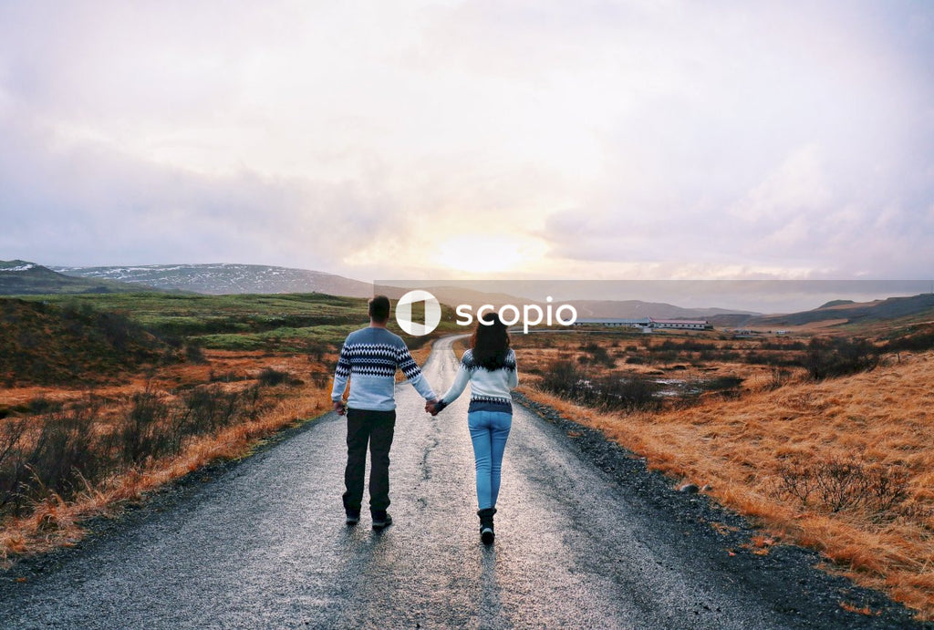 Back view of man and woman wearing sweaters and walking holding hands in sparse outdoor